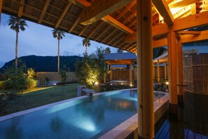 Une piscine avec une terrasse en bois, entourée de palmiers et avec une montagne en arrière-plan.
