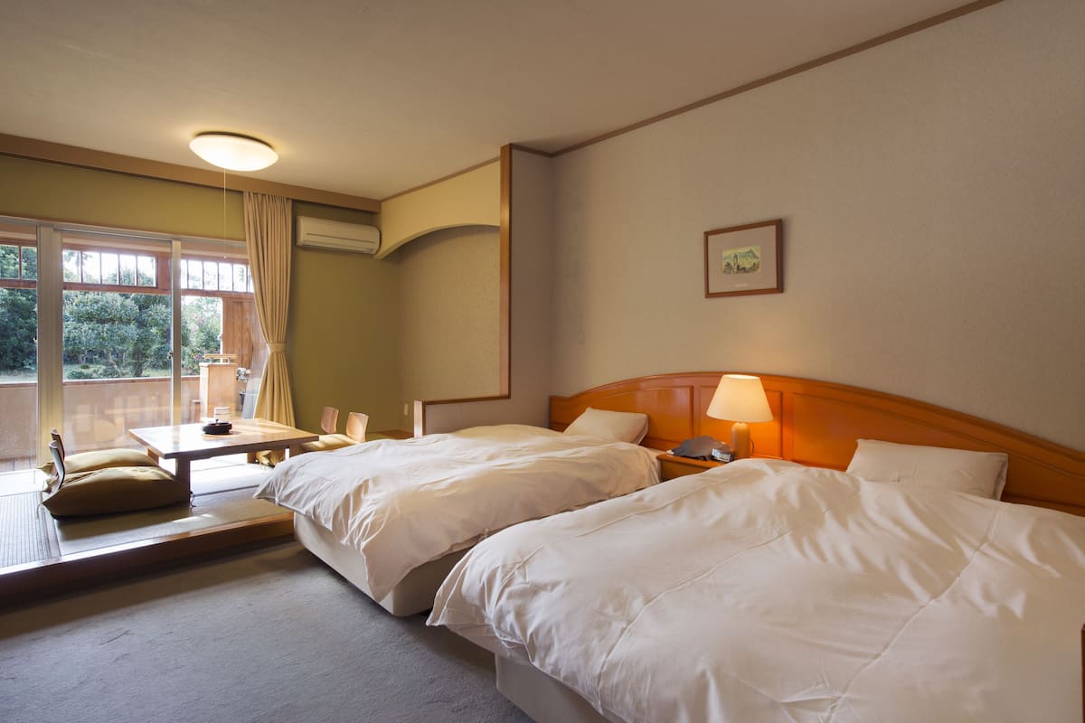 Habitación de hotel con dos camas, una mesita y un balcón con cortinas.
