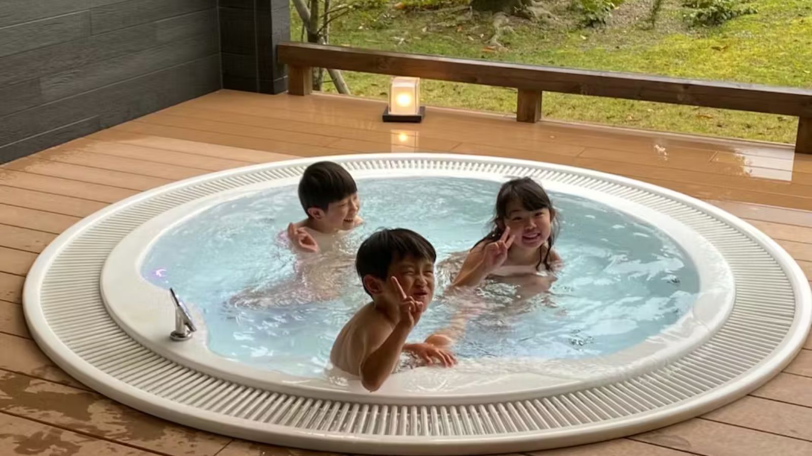 Un jacuzzi con tres personas, rodeado por una terraza de madera y una barandilla.