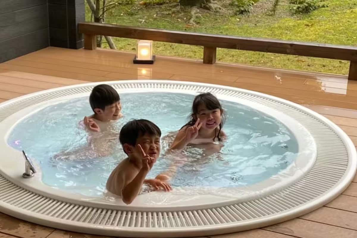Un jacuzzi con tres personas, rodeado por una terraza de madera y una barandilla.