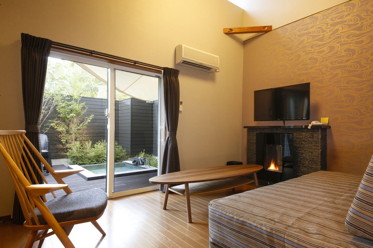 Una sala de estar con un sofá, una silla de madera, una mesa, una chimenea y un televisor fijado en la pared.