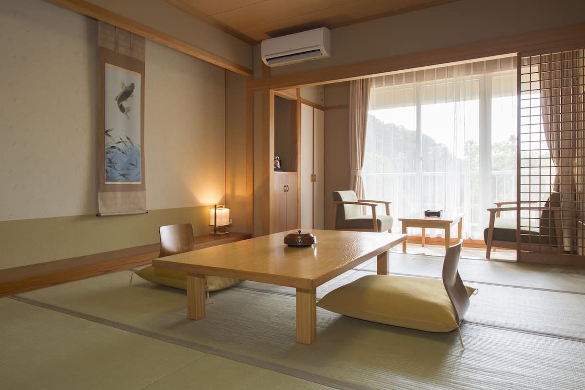 Una habitación japonesa tradicional con suelo de tatami, una mesa baja, sillas y una puerta corredera.