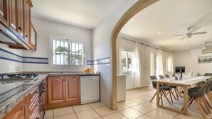 Una cocina con armarios de madera, lavavajillas y ventana. Hay un comedor con mesa y sillas.