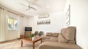 Una sala de estar con sofá, una mesa de centro, televisor y ventilador de techo.