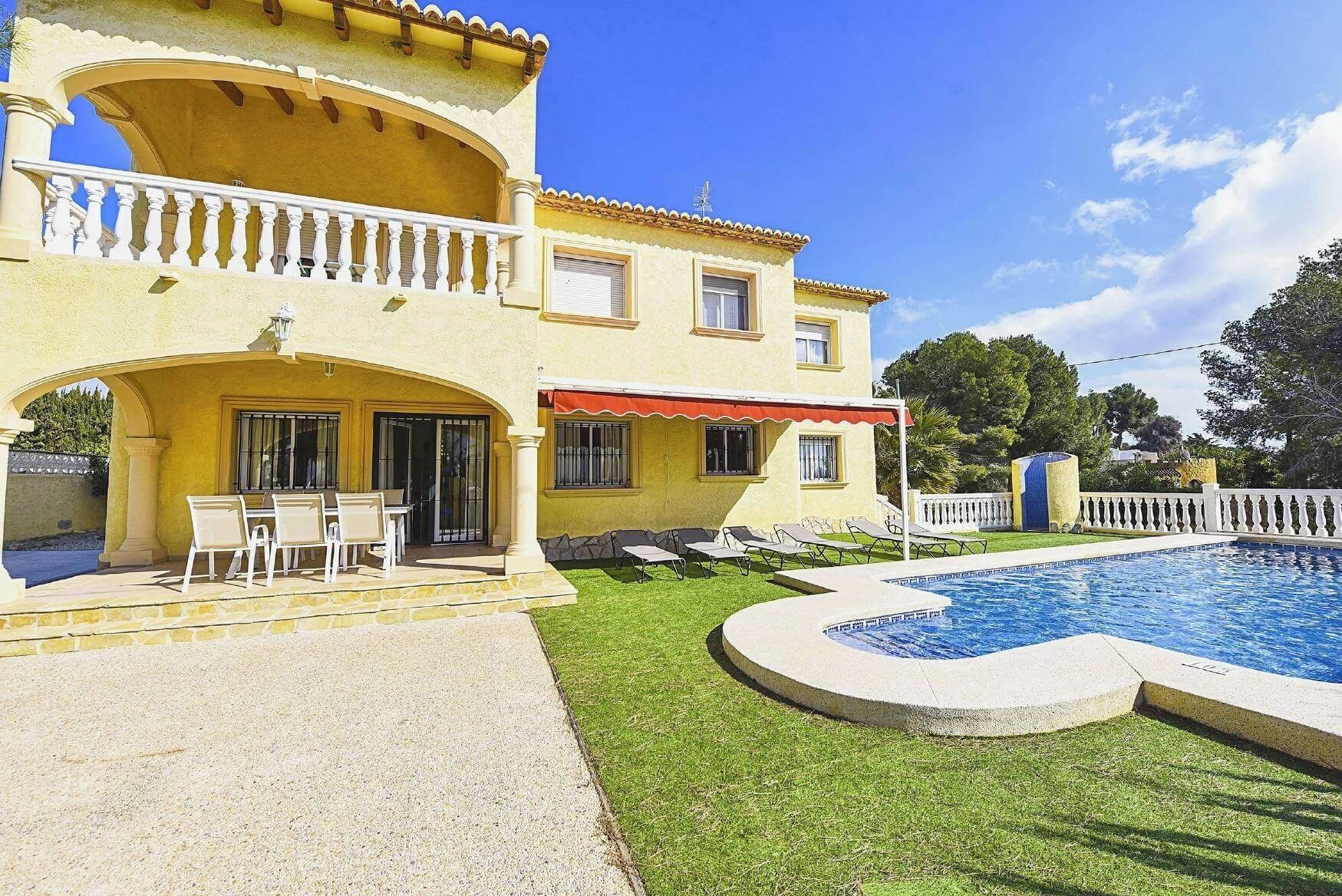 A two-story house with a swimming pool, a patio with chairs, and a covered outdoor seating area.