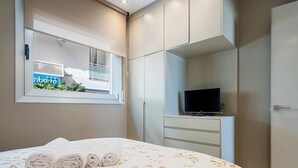 A bedroom with a bed, a TV on a stand, and a window with a view of a building.