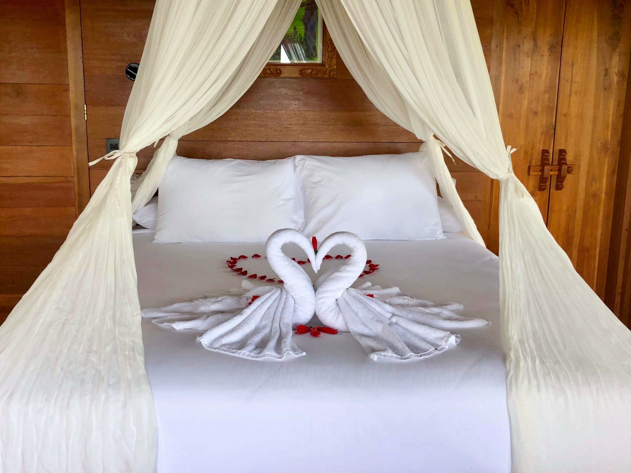 A bed with a canopy, white bedding, and two swan-shaped towels.