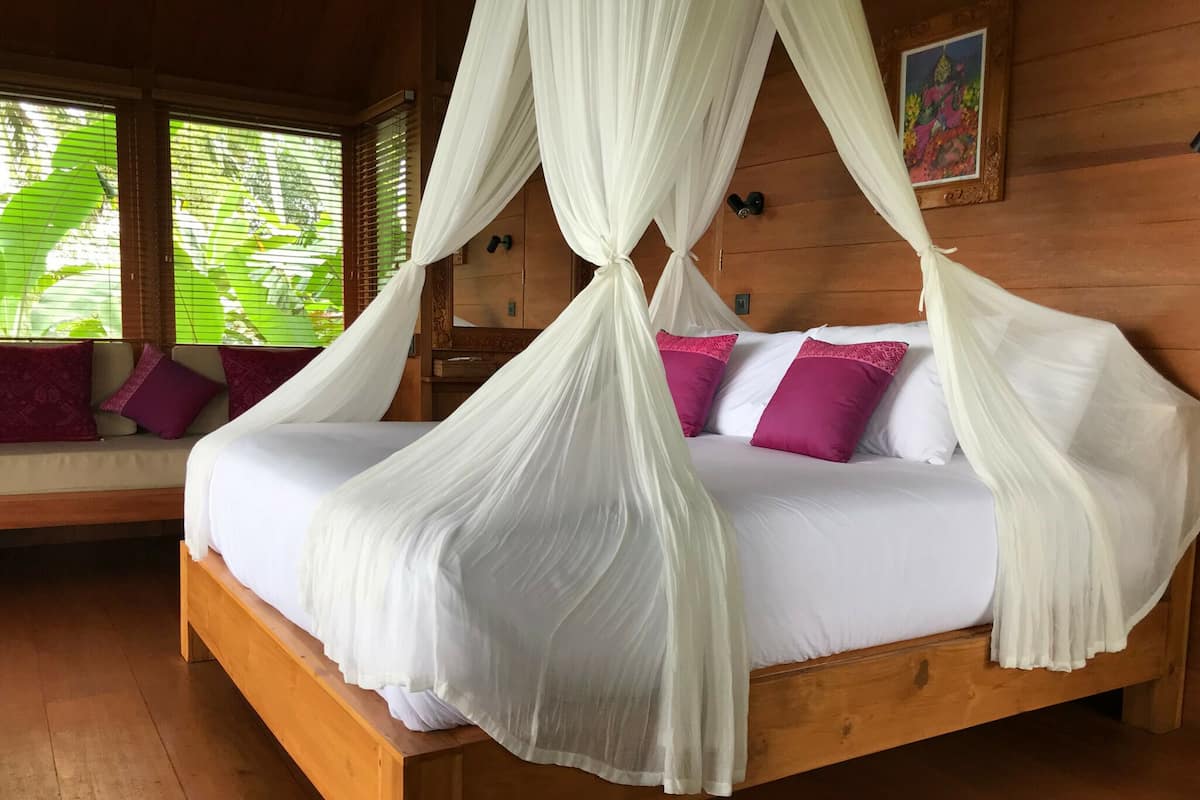 A wooden bed with a canopy, white bedding, and purple pillows.