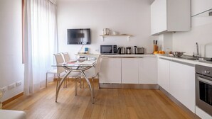 Une cuisine de taille réduite, avec des meubles blancs, un four à micro-ondes, une machine à café et un évier.