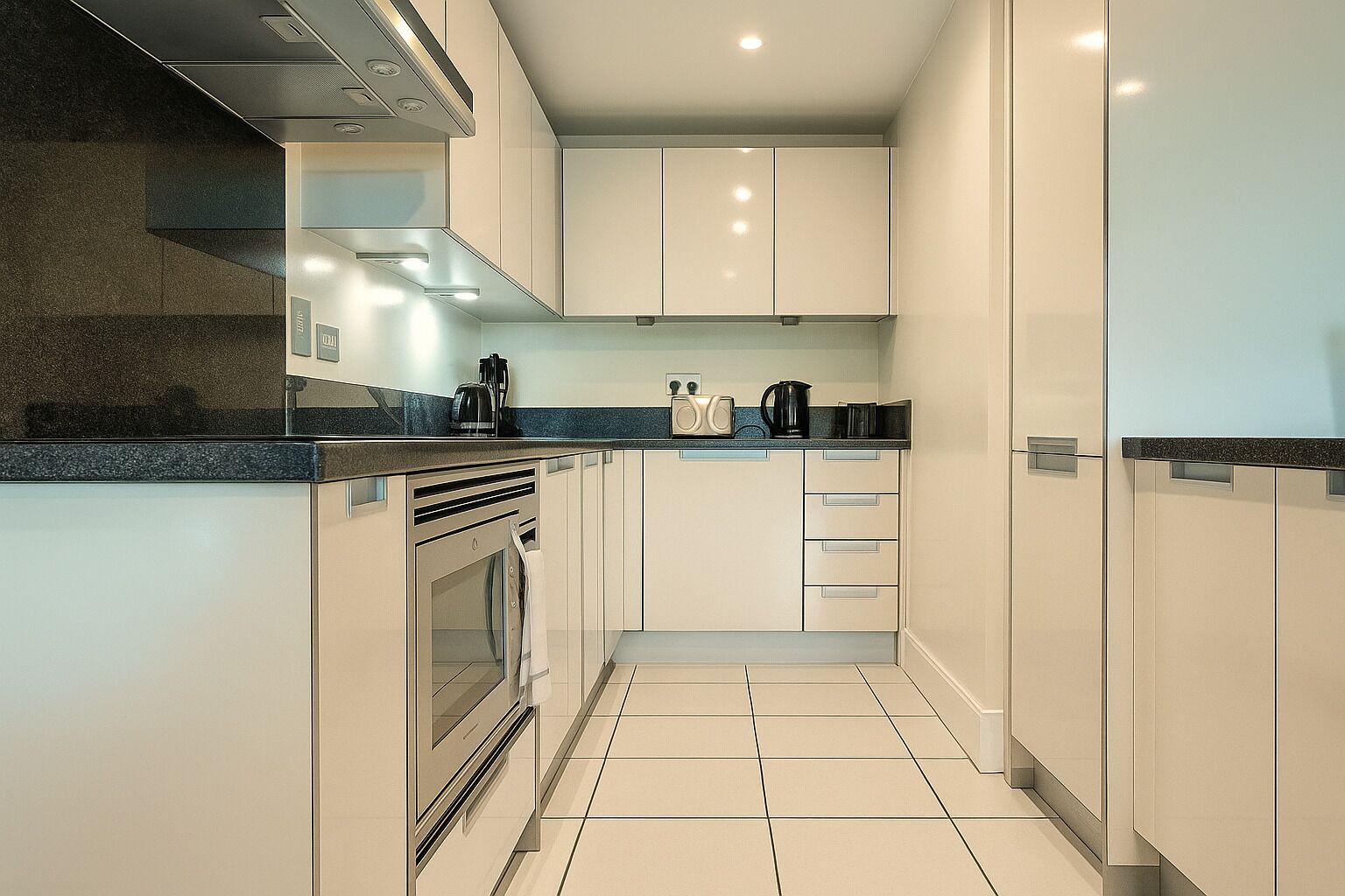 A modern kitchen with white cabinets, a black countertop, and a tiled floor.