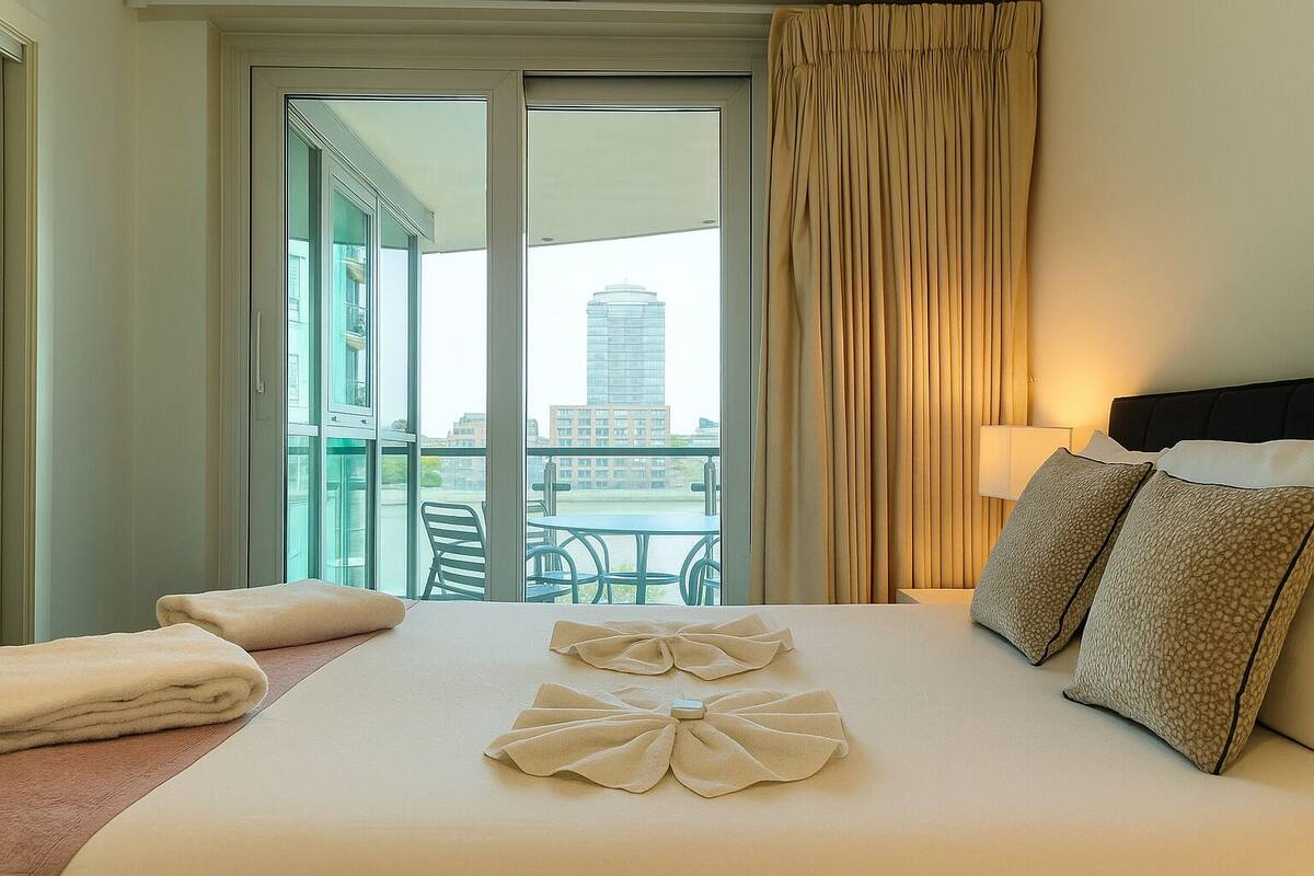 A hotel room with a large bed, a balcony with a view of buildings, and a table with chairs outside.