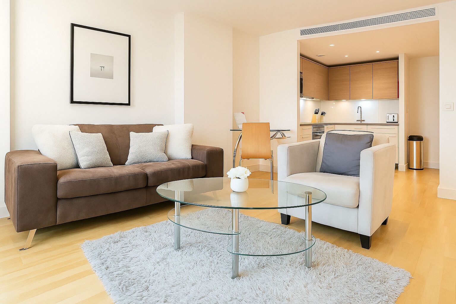 A modern living room with a brown sofa, a white armchair, and a glass coffee table.