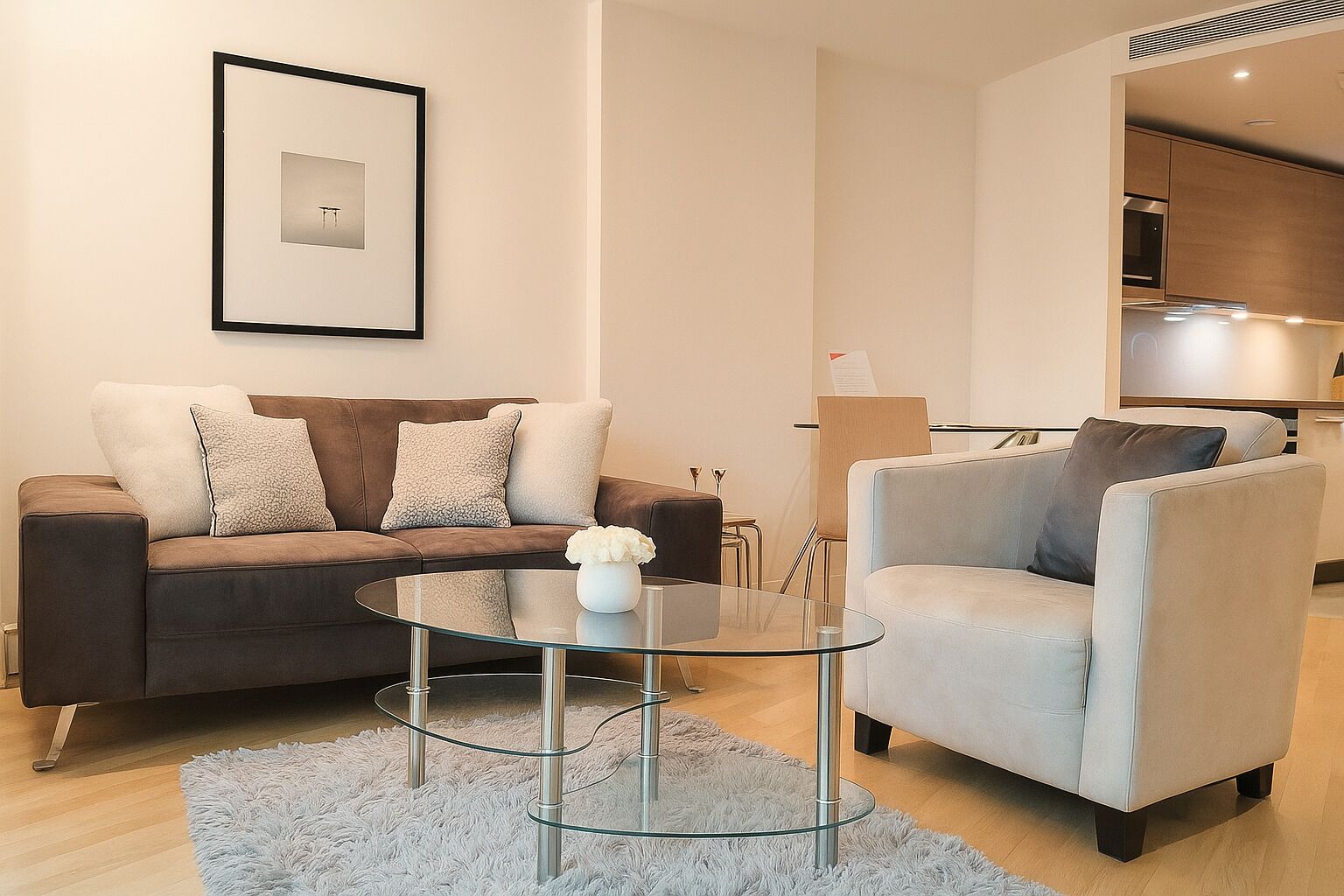 Een moderne woonkamer met een bruine bank, een lichtgrijze fauteuil en een glazen salontafel.