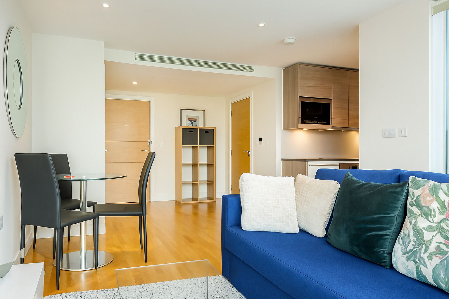 A modern living room with a blue sofa, a dining table with chairs, and a kitchen area in the background.
