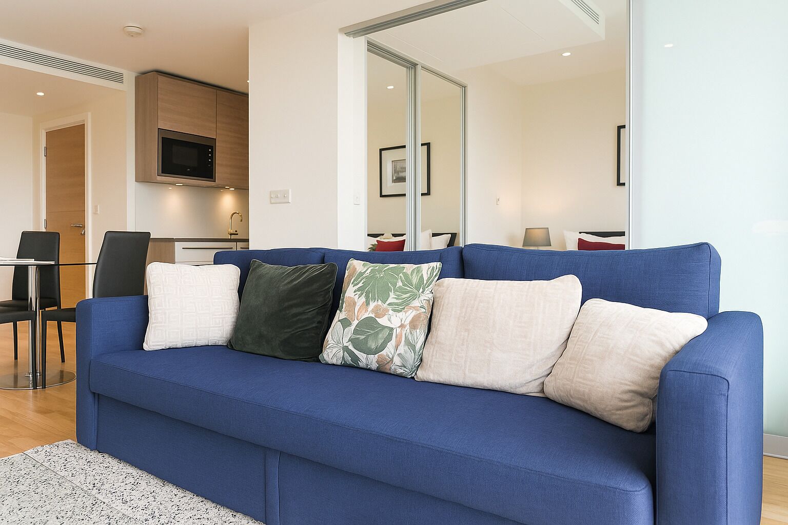 Un soggiorno moderno con un divano blu, un tavolino in vetro e un'area cucina sullo sfondo.