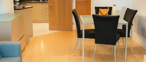 A modern kitchen with wooden cabinets, a dining area with a table and chairs, and a black exercise mat in the foreground.