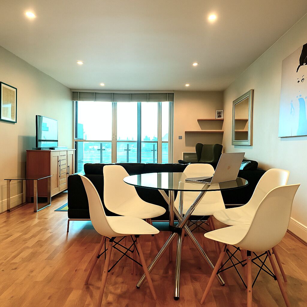 A modern dining area with a glass table, white chairs, and a laptop on the table.