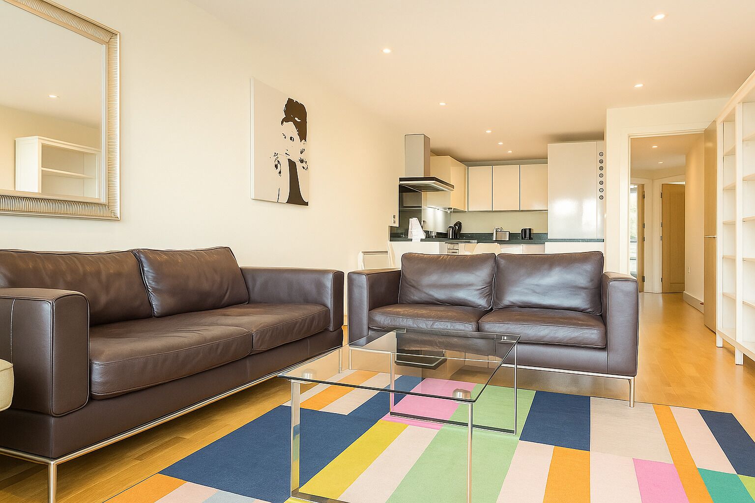 Ein modernes Wohnzimmer mit zwei Ledersofas, einem Glastisch und einem bunten Streifen Teppich.