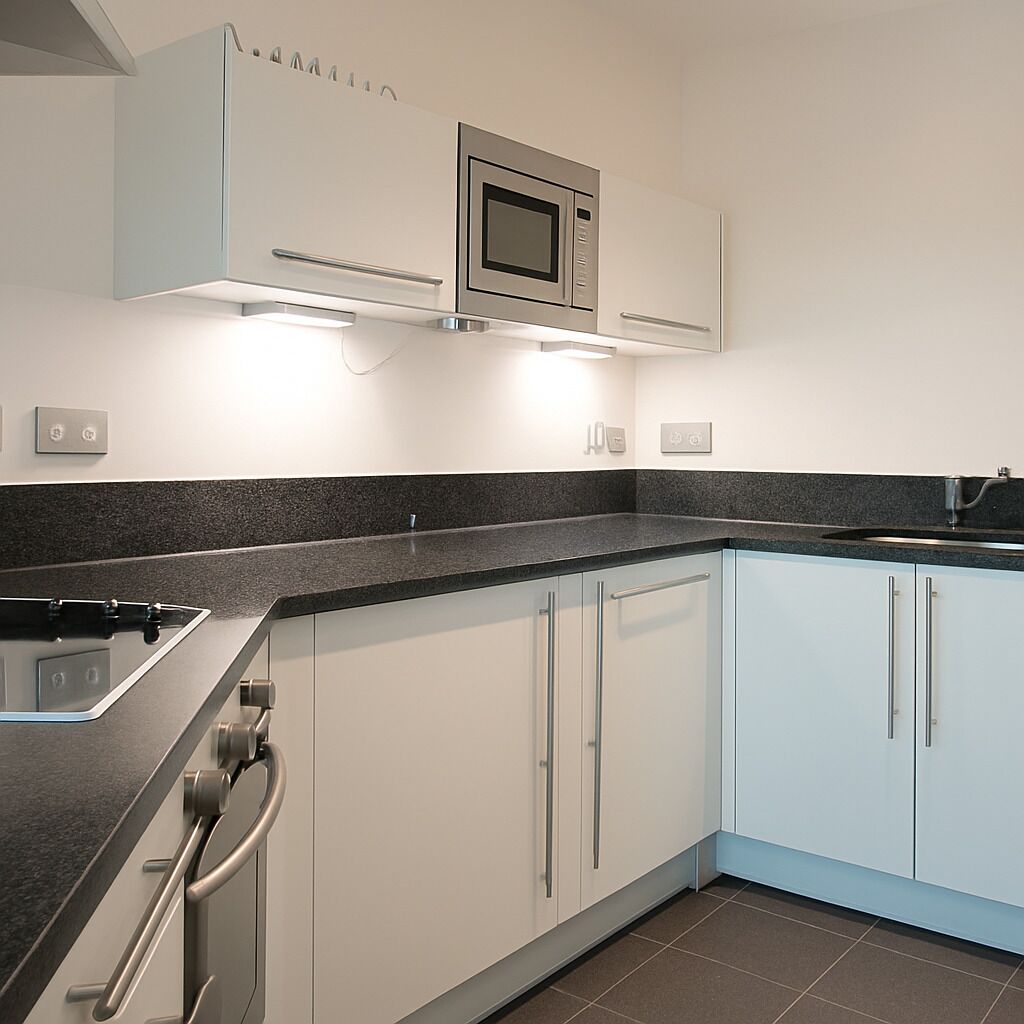 A modern kitchen with white cabinets, a black countertop, and a stainless steel microwave.