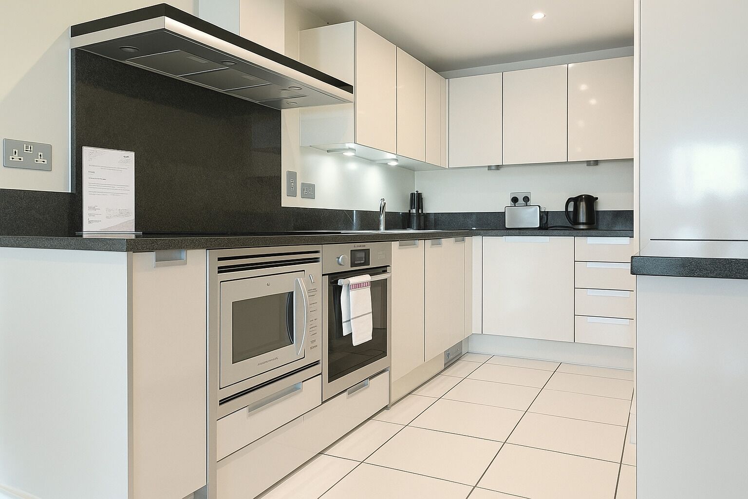 A modern kitchen with stainless steel appliances, white cabinetry, and a black countertop.