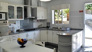 A modern kitchen with white cabinets, a granite countertop, a gas stove, and a window providing natural light. - Perched above village, ocean views | Jardim Mar (Ponta do Sol)