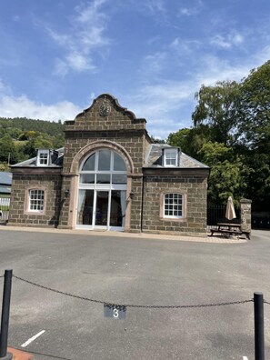 Un edificio de piedra con una gran entrada en arco, un reloj sobre la puerta y una mesa de picnic en el exterior.