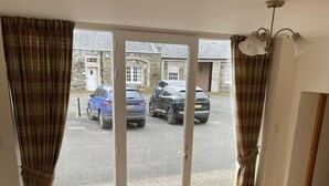 A dining area with a wooden table and chairs, a view of parked cars through a glass door, and a stone building in the background. - Stay somewhere unusual , Peaceful central location, sleeps 4, Pets Welcome. (Perth)