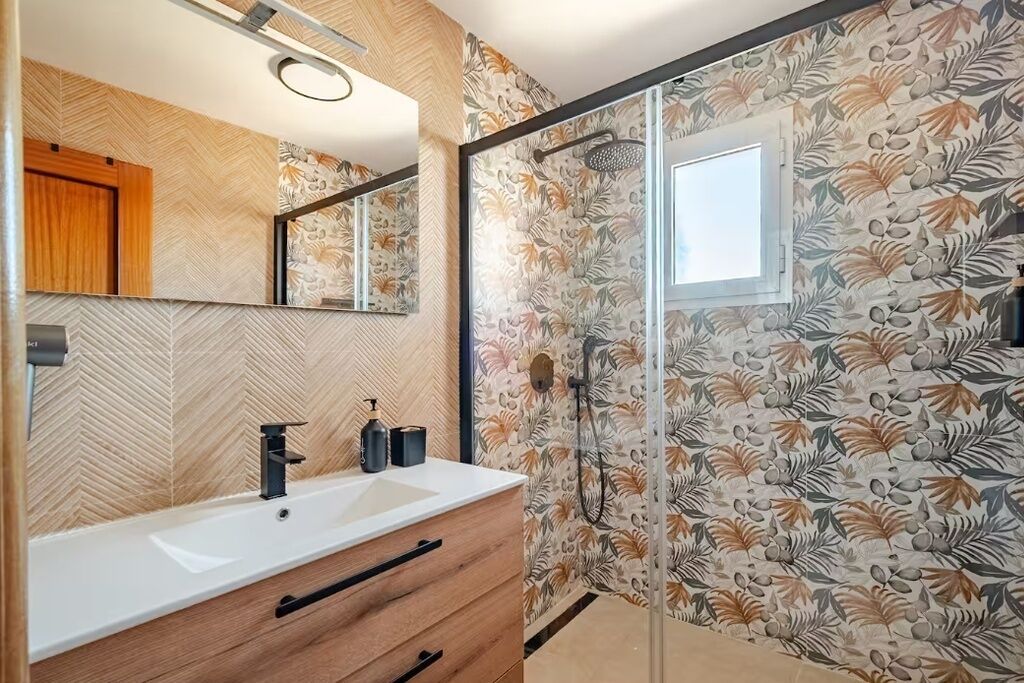 Een badkamer met een witte wastafel, een houten kastje en een douche met een glazen deur.