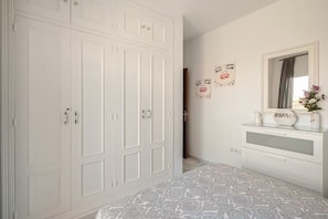 Ein Schlafzimmer mit großem Kleiderschrank, Schminktisch mit Spiegel und einem geblümten Bettüberwurf.