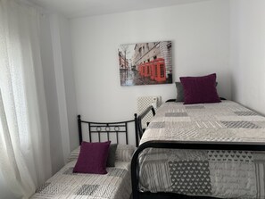 Ein Schlafzimmer mit einem Bett, zwei Kissen, einem Kopfteil, einem Wandbild und einem Fenster mit Vorhängen.