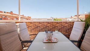 En terrasse med et bord og stole, en murstensmur og frit udsyn til bygninger i baggrunden.