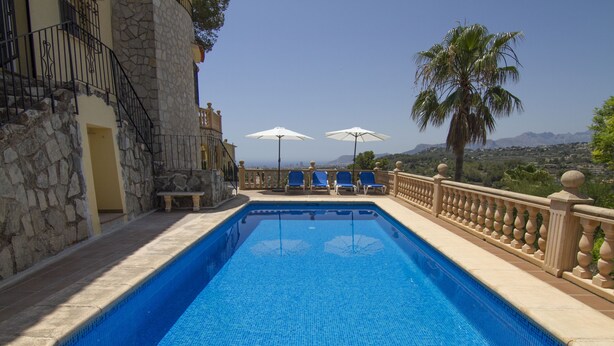 A swimming pool with blue tiles, surrounded by stone walls and a balcony with blue chairs and white umbrellas. - Villa Aline between Moraira and Calpe, private pool, WIFI, air conditioning, (Benissa)