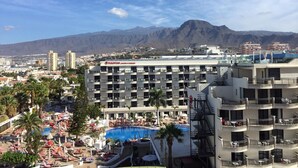 Um hotel com piscina, várias varandas e uma montanha ao fundo.