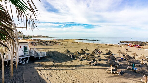 Uma praia com guarda-sóis, espreguiçadeiras e posto de salva-vidas.