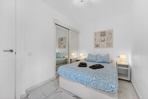 A bedroom with a bed, bedside tables, a mirror, and a wall art piece.
