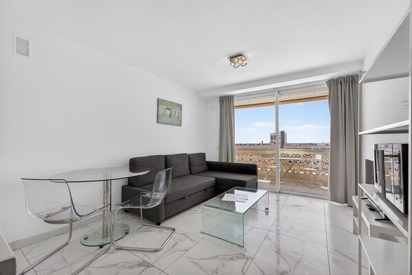 A modern living room with a glass coffee table, a grey sofa, and a glass dining table with chairs.