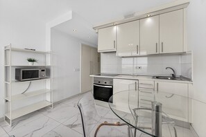 A modern kitchen with white cabinets, a microwave, and a glass dining table.