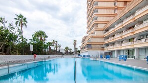 Piscina com vista desobstruída da área circundante, incluindo um edifício com varandas e palmeiras.