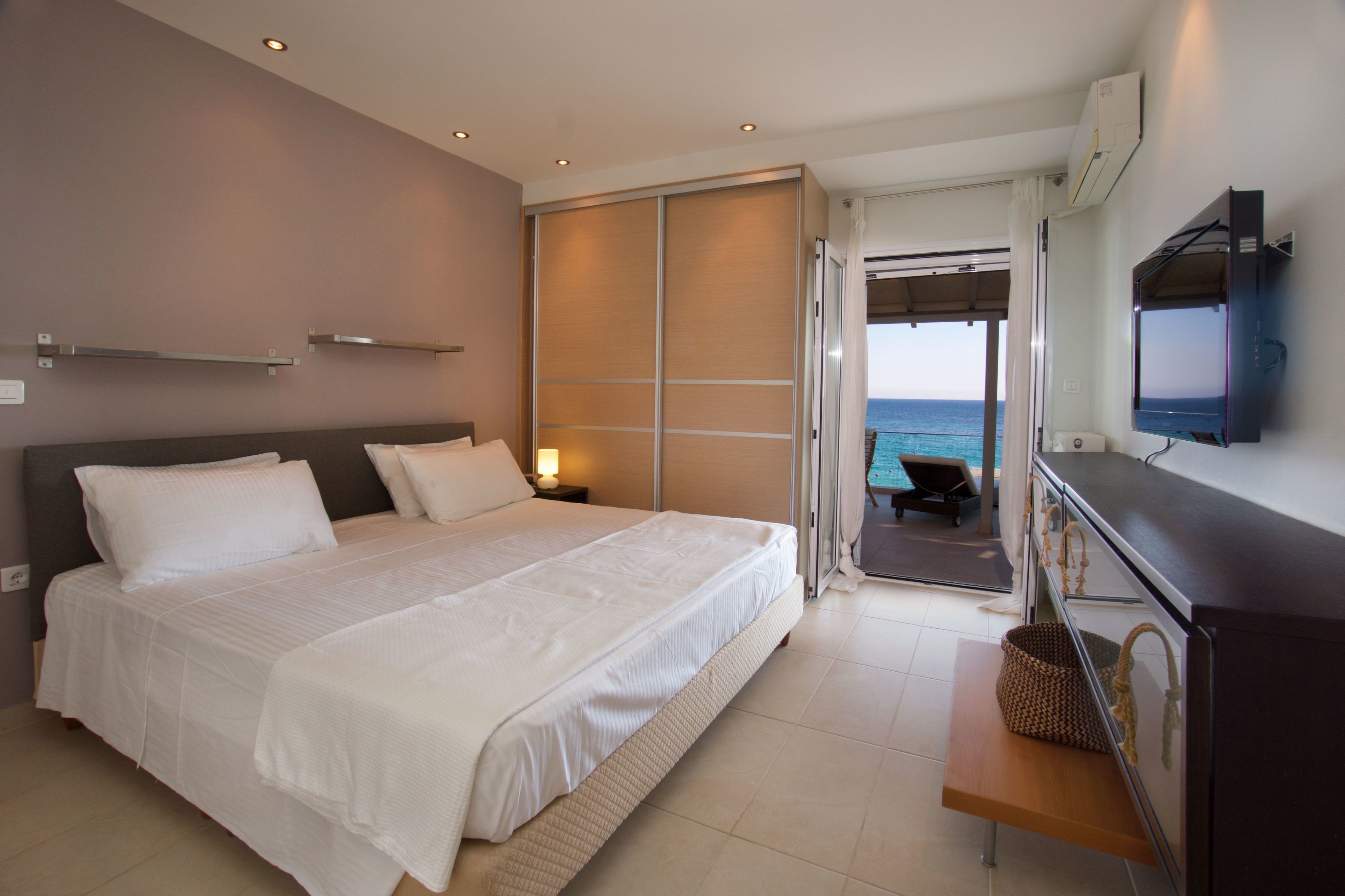 A bedroom with a bed, a TV, a desk, and a view of the sea.
