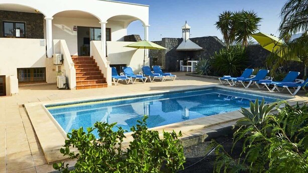 Ein modernes Gebäude mit Pool, blauen Liegestühlen und einer Treppe zum Eingang.