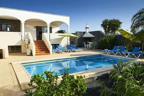 A modern building with a swimming pool, blue lounge chairs, and a staircase leading to the entrance. - Casa Indiana - Large Family Villa by Villas Now (Playa Blanca)