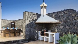 Eine Außenpatio mit Steinmauern, einem Grill und einer Essecke mit Stühlen und Tischen.