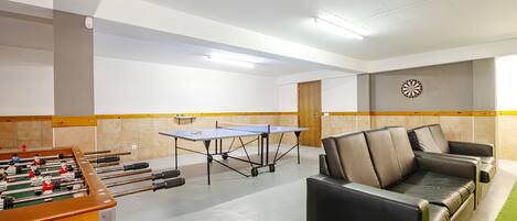 Una habitación con mesa de fútbol de mesa, mesa de ping pong y un sofá.