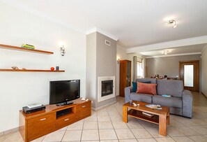 Ein Wohnzimmer mit Fernseher, einer Holzunterhaltungsecke, einem grauen Sofa und einem Kamin.