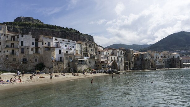Une ville côtière dotée de bâtiments historiques le long du front de mer, d’un ciel dégagé et où les habitants profitent de la plage.