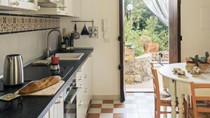 Une cuisine avec un carrelage à motifs, un coin repas avec une table et des chaises, et une vue sur le jardin par une porte ouverte.