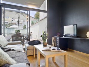 A modern living room with a sofa, a coffee table, a TV on a black stand, and a balcony with a table and chairs. - My Space Barcelona Loft for temporary rentals with terrace and swimming pool (Barcelona)