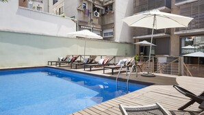 Una piscina en la azotea con sillas de descanso y sombrillas, rodeada de edificios.