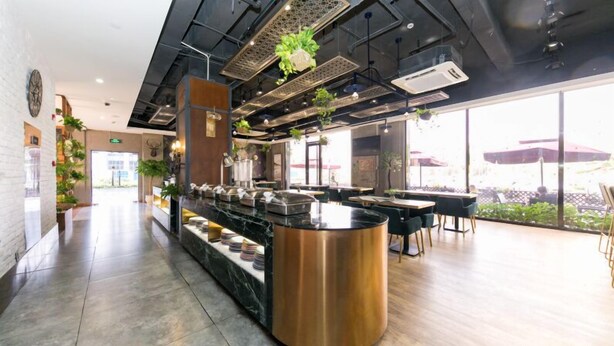 Ein modernes Restaurant mit einer zentralen Theke, Sitzbereich und großen Fenstern mit Blick ins Freie.