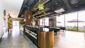 A modern restaurant with a central counter, seating area, and large windows offering outdoor views.